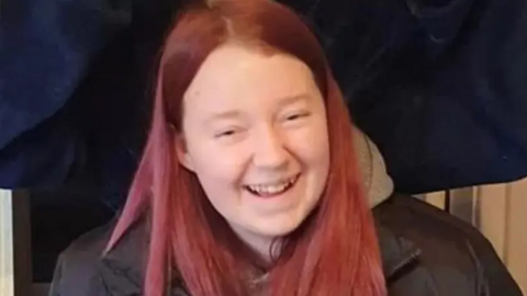Teenage girl with pink care and black jacket. She is smiling at the camera.
