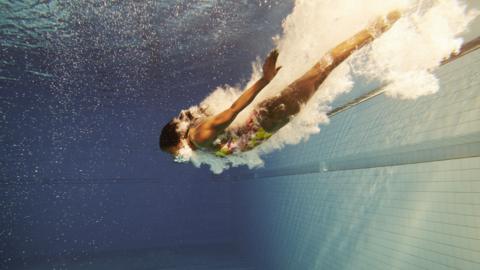 Woman dives into a swimming pool, clouded in bubbles