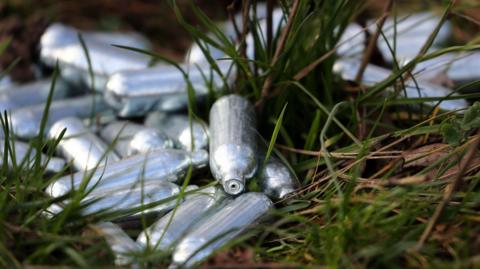 Discarded grey canisters of nitrous oxide, or laughing gas, lying in the grass. 