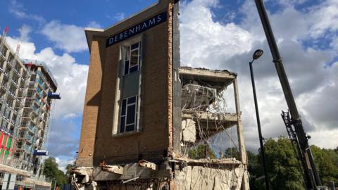 A front facade is all that remains of the former Debenhams store - which also has the store's logo on it. The back of the building is mostly demolished.