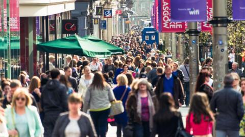 Crowds of people passing shops on Buchanan Street, Glasgow on a bright day.