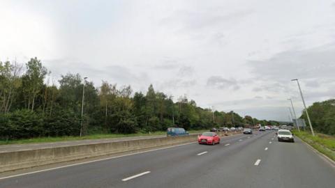 Section of road on A1 southbound near Metrocentre. Trees are on the side. Several cars are on the road driving. 