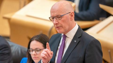 John Swinney stands up in the Scottish Parliament to deliver his speech