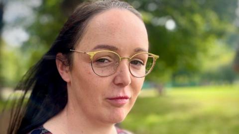 a woman with long brown hair is wearing gold-framed glasses