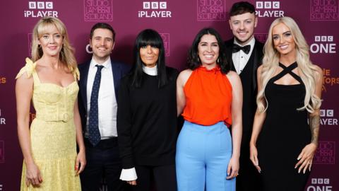 Traitor finalists Francesca, Alexander, Charlotte, Jake and Leanne pose with host Claudia Winkleman against a purple background and smile at the camera 