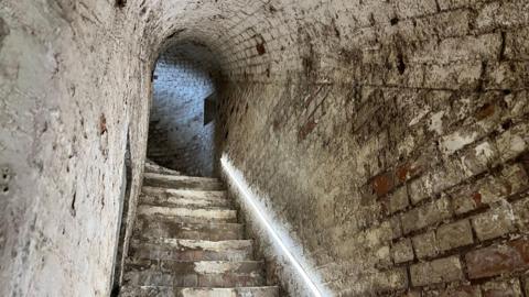 Stairs leading up to a gunning position in Newhaven Fort. The stairs are surrounded by several feet of concrete of bricks and there is an LED strip of lights on one of the walls.