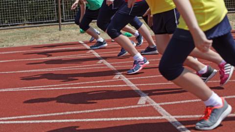 Athletes setting off from the white start line on a red running track.