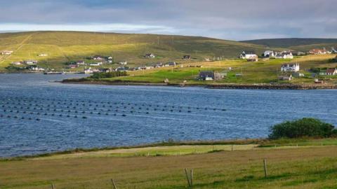 Hills and houses in Shetland, with body of water in the foreground.