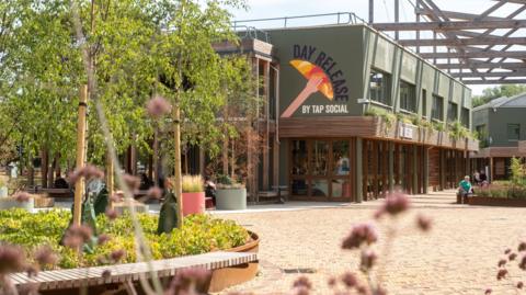 An exterior view of Tap Social's Day Release at Milton Park's Signal Yard. Some people are seating on benches in front.