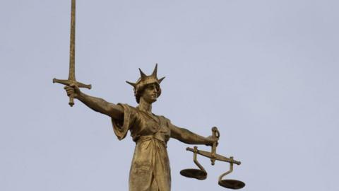 Gold coloured scales of justice statue with sword in one hand and scales in other hand. 