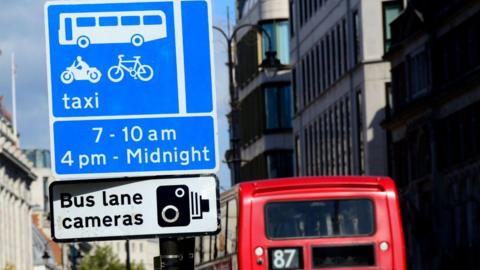 Bus lane camera sign with a the top of a a number 87 London bus shown