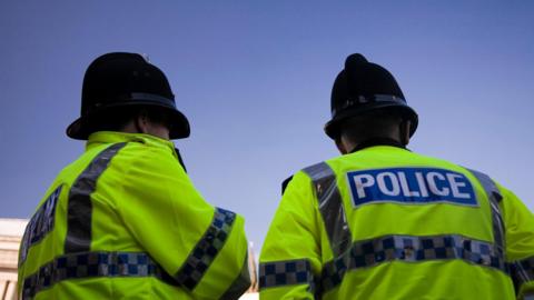 Two police officers stand together in fluorescent uniform and helmets looking out on a clear blue sky