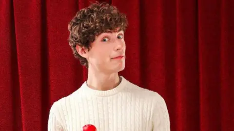 A man with brown hair wearing a white jumper