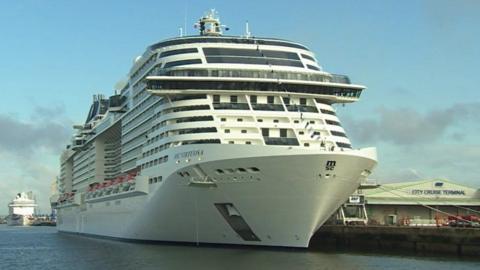 White cruise ship berthed with ropes to its left side onto the docks.