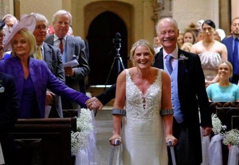 A blonde woman in a white wedding dress makes it down the aisle on clutches.