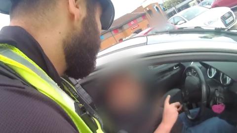 A police officer standing next to a car with a driver inside.