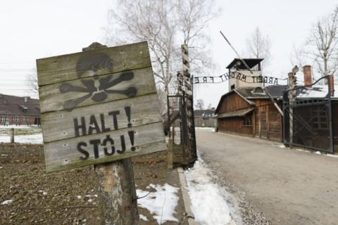 a sign with a skull and crossbones reads 'halt! stoj' next to the entrance of auschwitz