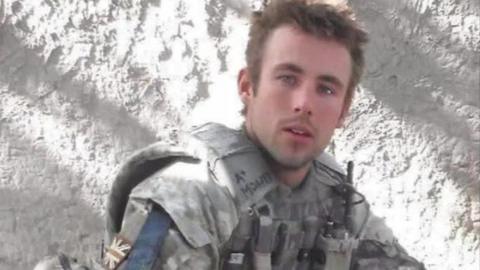 A head and shoulders shot of Sam Morgan wearing a uniform. He's a young man with short brown hair and is not smiling 