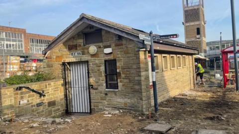 A single story toilet block with a gated doorway and a row of windows along one side