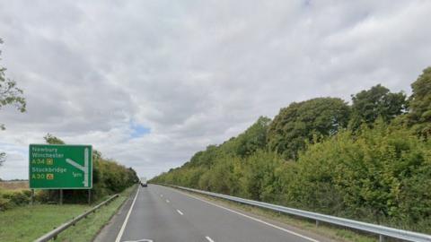 Dual carriageway with vehicles seen in the distances - road barrier and hedging on the right and roads sign to the left