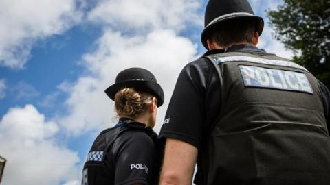 Two Sussex police officers turn away from the camera and look up at blue skies