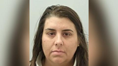 Police custody image of Keira Burton who has long dark brown hair and eyes. She is wearing a cream fleece.