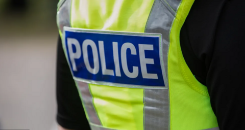 The back of a yellow British police officers vest with the word police in bold white lettering against a blue rectangle.