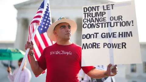 A protester hold a sign saying 'don't give trump more power' in front of the supreme court.