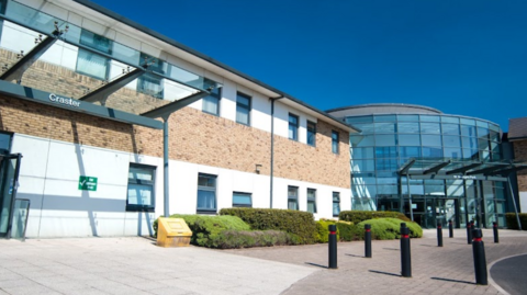 An exterior view of the hospital with a curved glass front surrounded by a long building.