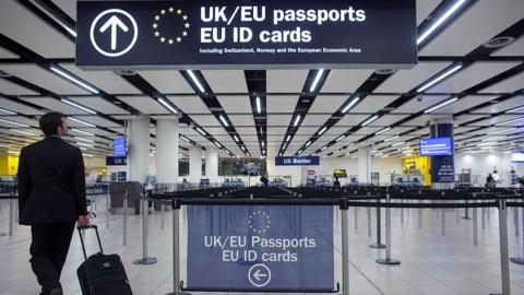 A man holding a suitcase walks past a sign for an EU passport queue at an airport.