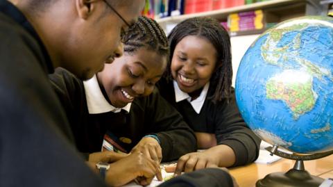 Three GCSE students in a school classroom work on a geography project with a globe on the table.