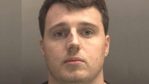 A mugshot of Thomas Hooton. He has short dark hair and is wearing a dark top.