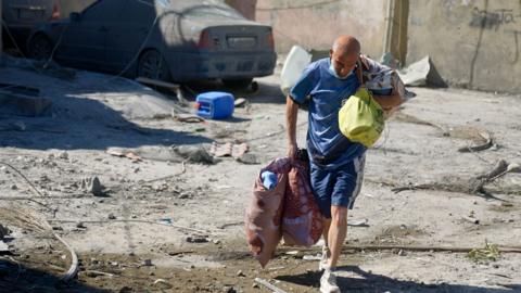 Mohammed Sukayneh picks his way through slabs of rubble and twisted metal, clutching a few plastic bags