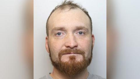 Mugshot of Marcin Janikowski. He is on a grey background and looking at hte camera with an orange moustache and beard. He has receding hairline.
