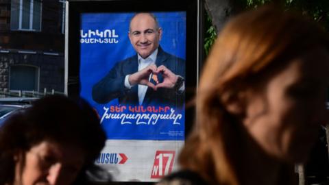 Street poster of a man wearing a blue suit doing a heart sign with his hands