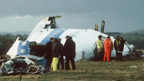 Emergency service personnel standing next to the fuselage of Pan Am flight 103 after it was downed over Lockerbie.