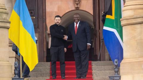 Ukraine's President Volodymyr Zelensky shakes hands with South African President Cyril Ramaphosa on steps outside a building. 
