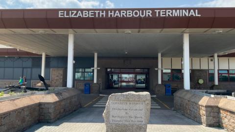 The front of the Elizabeth Harbour Terminal building with a large poritco bearing the name of the building and a stone commemorating the opening of the harbour by Queen Elizabeth II in 1989