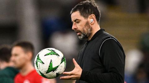 Tiernan Lynch in a black outfit and wearing a white earbud, with a football