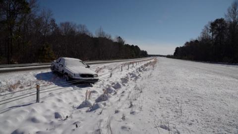 A car is on the side of the highway with snow on the ground.