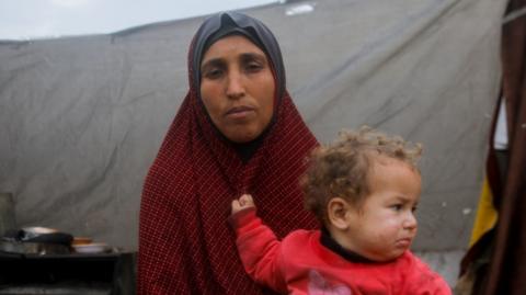 A Palestinian woman holds her child outside their makeshift shelter in Jabalia, northern Gaza