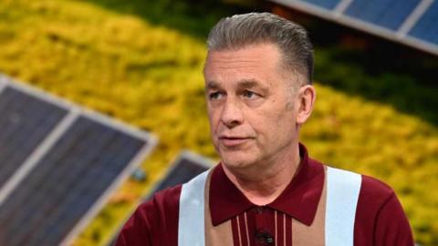 Chris Packham seen in a still of a TV clip - he is conserving with the host, who is not in shot, and is seen looking to the right. He is wearing a polo shirt