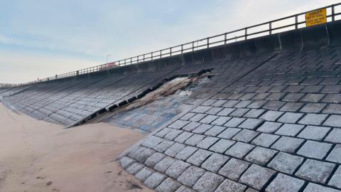 Damaged sea wall defences at Aberdeen beach, much of the stonework is missing, above the sand, and the promenade is above.