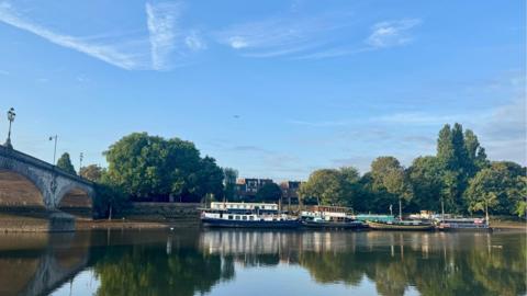 Wispy cloud and pale blue skies over a calm river.