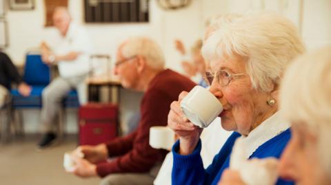 A close up shot of an older woman drinking tea with friends.