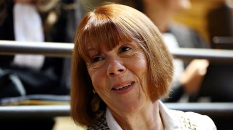 A woman with red-coloured hair and a fringe smiles