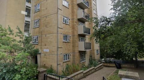 A Google Street View image shows the base of Berkeley House. Taken in summer, the tower block is surrounded by green trees. 