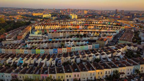 The sun rises over colourful houses in Totterdown, Bristol, creating a golden glow on the rooftops. 