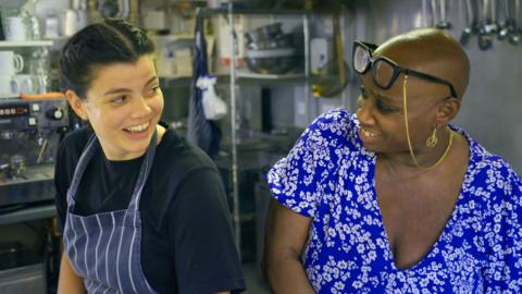 Andi Oliver laughs with a young chef in a kitchen