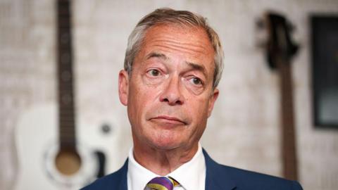 Nigel Farage in a close-up, wearing a blue suit, white shirt and stripe tie.